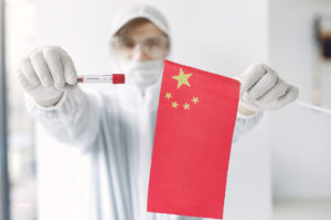The scientist in coverall suit with a coronavirus sample and Chinese flag